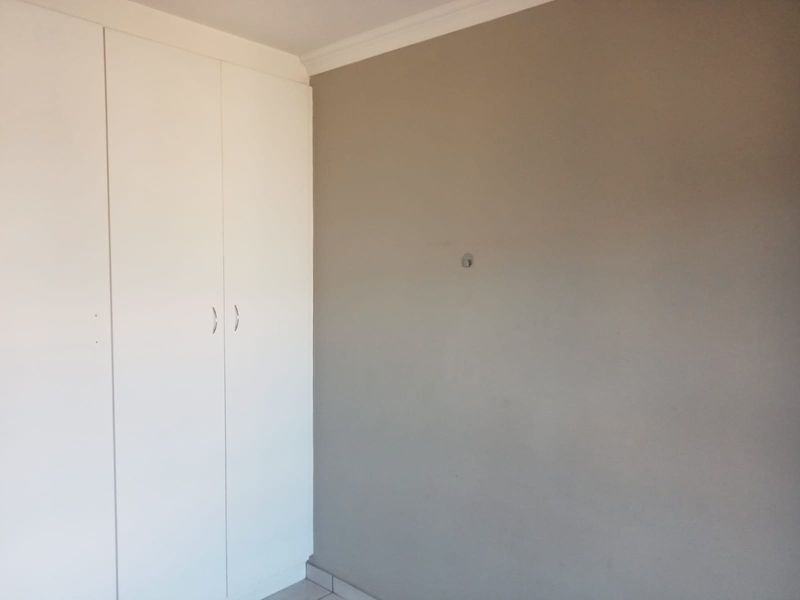 A clean, empty bedroom featuring neutral wall tones, tiled flooring, and white built-in cupboards with modern hardware.