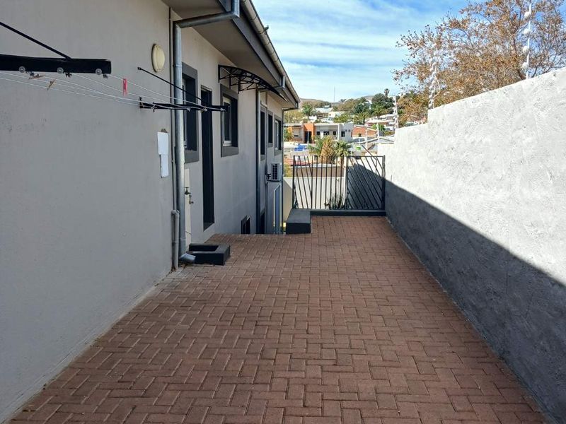 A paved side walkway featuring a boundary wall with electric fencing, guttering, and wall-mounted utility fixtures.