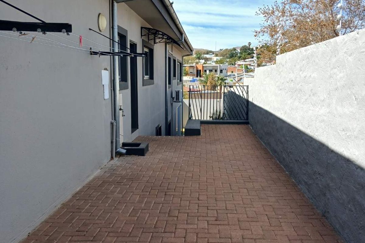 A paved side walkway featuring a boundary wall with electric fencing, guttering, and wall-mounted utility fixtures.