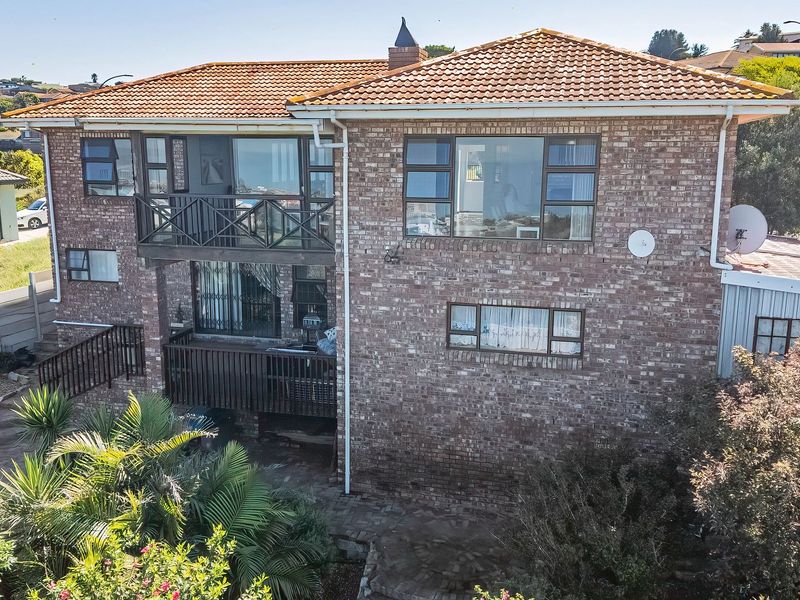 Rear elevation of a double-story brick house featuring a tiled roof, upper-level balcony, and paved patio area set within a landscaped garden.