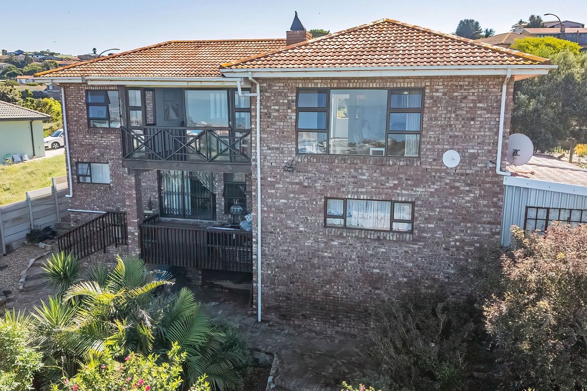 Rear elevation of a double-story brick house featuring a tiled roof, upper-level balcony, and paved patio area set within a landscaped garden.