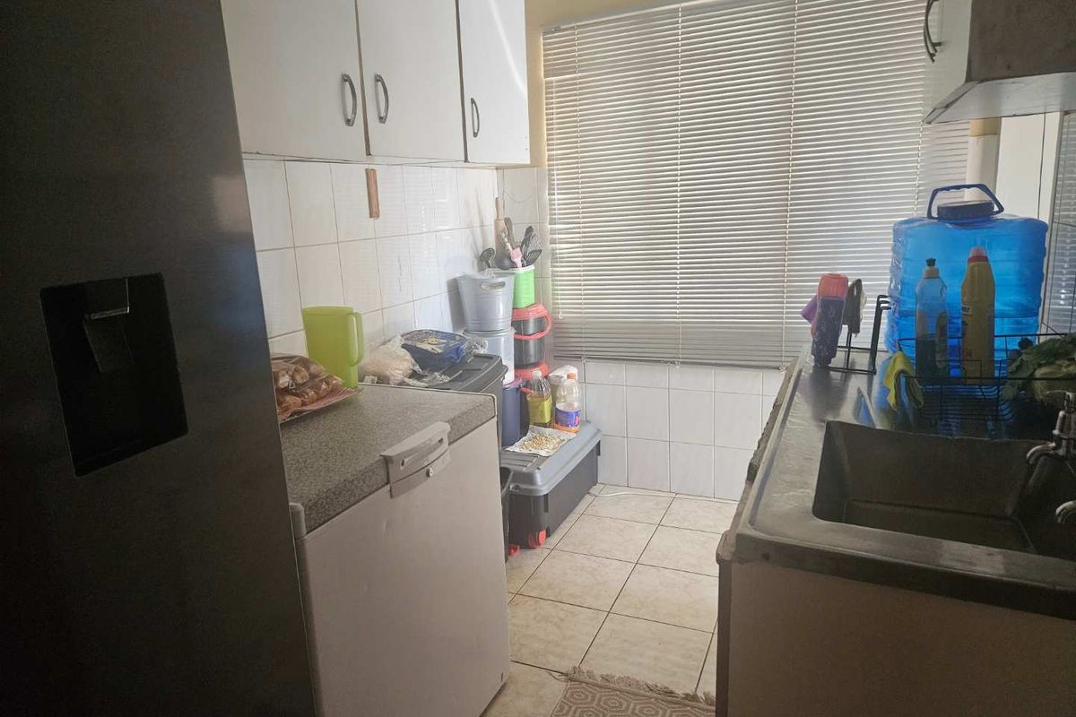 A compact kitchen area featuring tiled walls, built-in cabinetry, and a stainless steel sink, offering a functional space for food preparation.