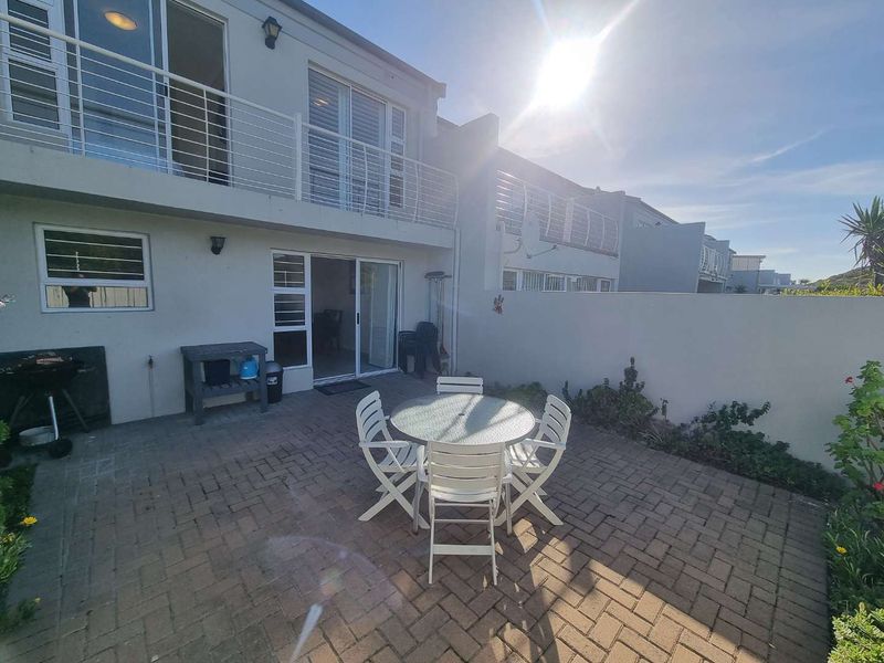 Rear view of the townhouse featuring a paved patio area, sliding door access, and an upper-level balcony with metal railings.
