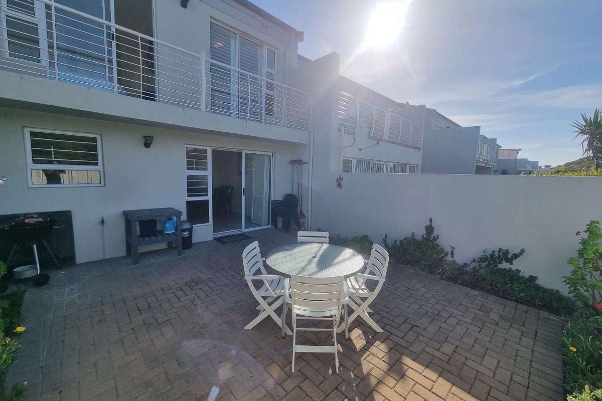 Rear view of the townhouse featuring a paved patio area, sliding door access, and an upper-level balcony with metal railings.
