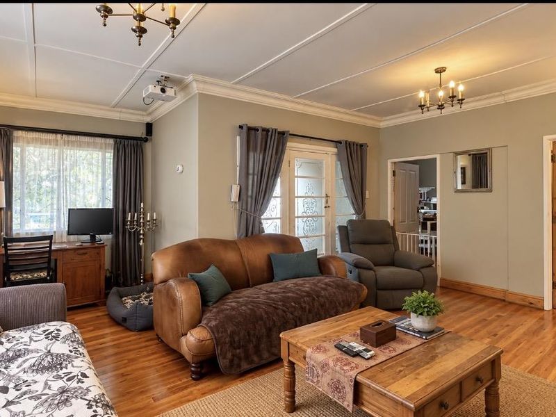 A spacious living room featuring polished hardwood flooring, classic crown molding, a panelled ceiling, and elegant french doors leading to an outdoor area.