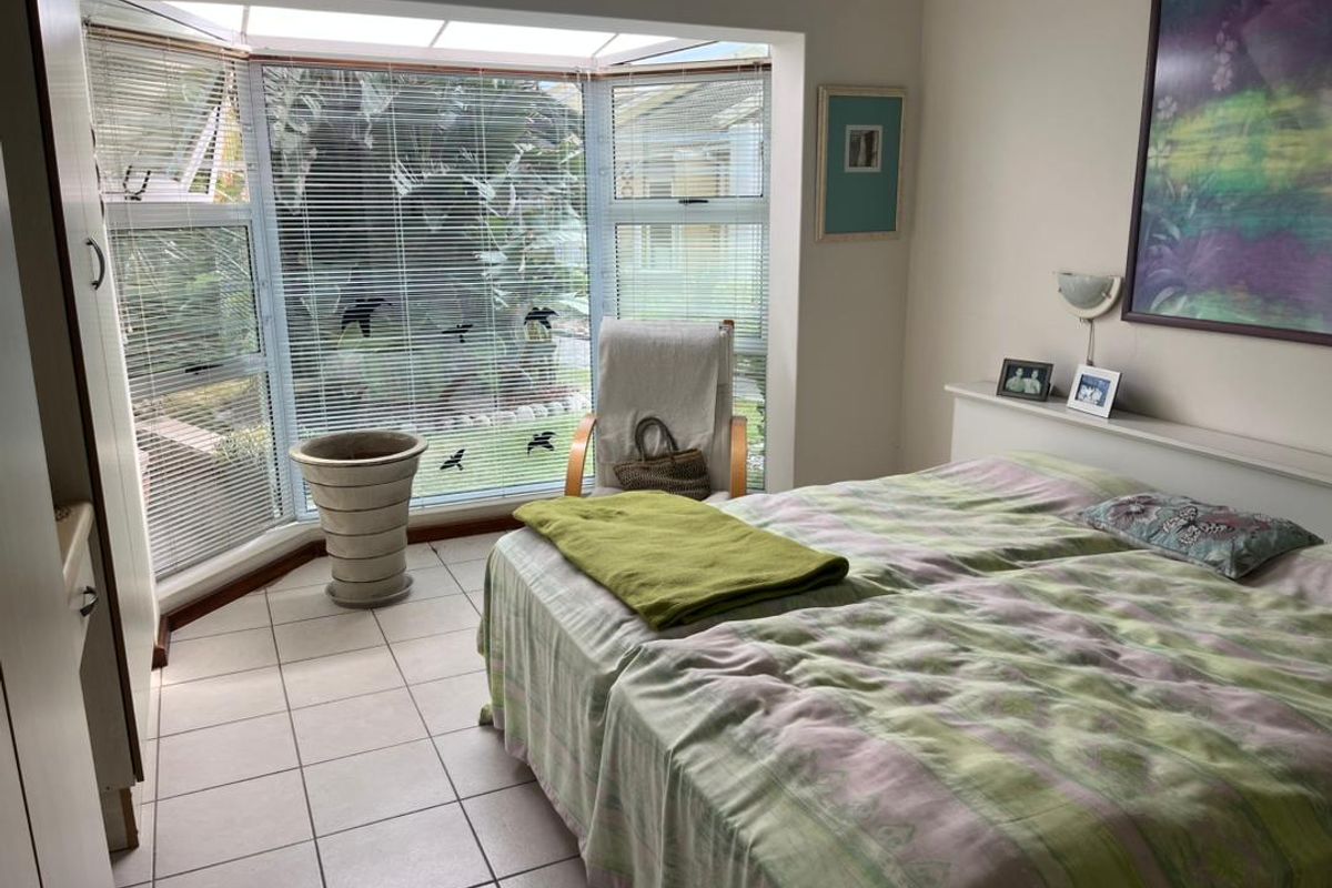 A bedroom featuring a large bay window with integrated blinds, tiled flooring, and a built-in headboard shelf.