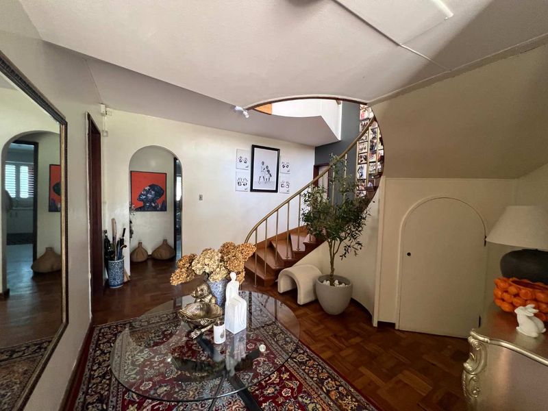 Spacious entrance hall featuring classic parquet flooring, a distinctive curved staircase with metal balustrade, and an arched doorway leading to adjacent living areas.