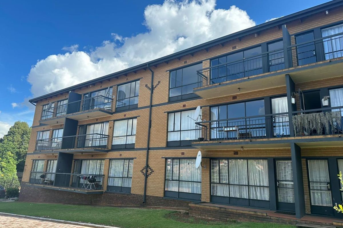Exterior view of a multi-story apartment building featuring brick facade, private balconies with metal railings, and large sliding glass doors.