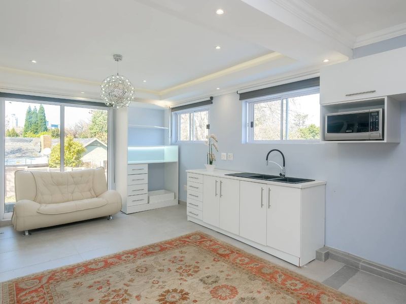 Bright open-plan living area featuring a modern kitchenette with built-in cabinetry, sink, and microwave, complemented by large sliding doors and recessed lighting.