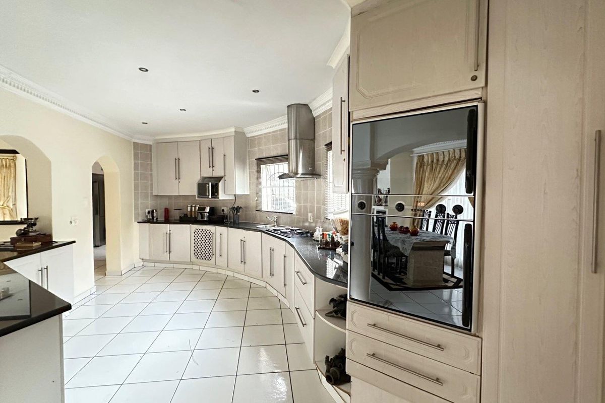 Spacious kitchen featuring curved cabinetry, granite countertops, built-in oven, stainless steel extractor fan, and tiled flooring.