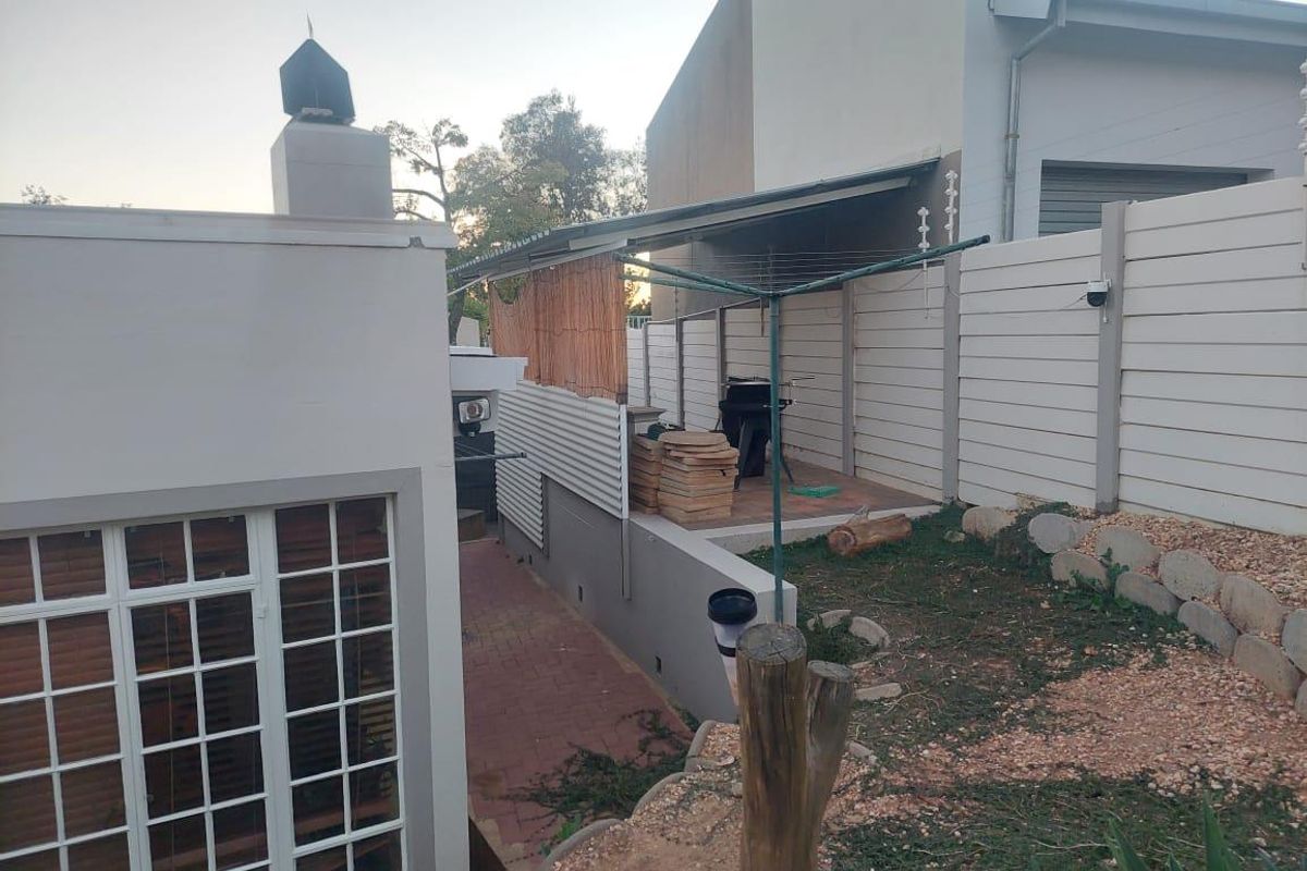 A rear exterior view of the townhouse featuring a paved patio area, a covered outdoor space, and a tiered garden section with perimeter fencing.