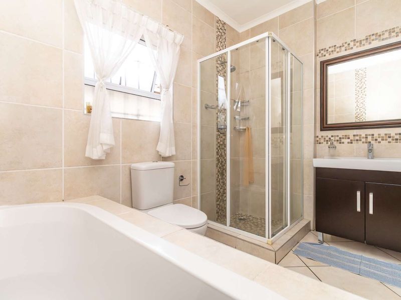 A well-maintained bathroom featuring a glass shower enclosure, a built-in vanity, a bathtub, and neutral tiled finishes with mosaic accents.