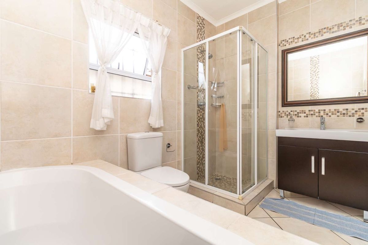 A well-maintained bathroom featuring a glass shower enclosure, a built-in vanity, a bathtub, and neutral tiled finishes with mosaic accents.
