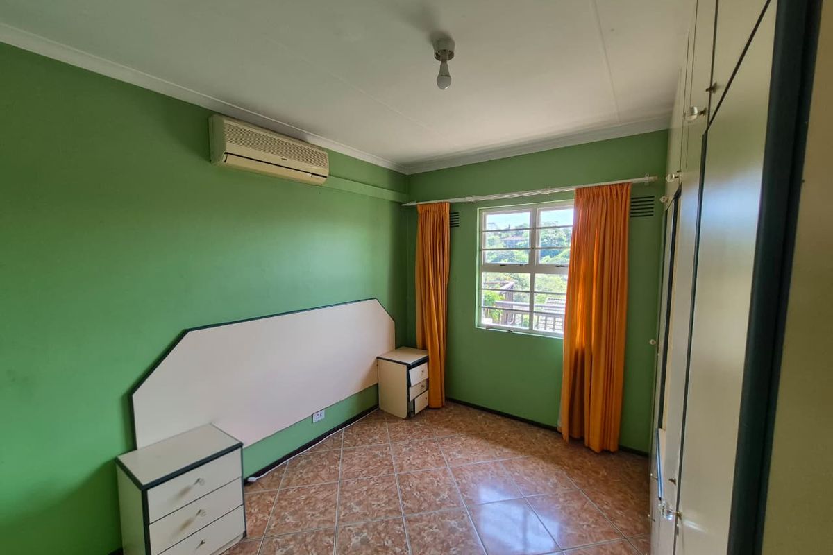 A bedroom featuring tiled flooring, built-in cupboards, and a wall-mounted air conditioning unit, offering a functional space with natural light.