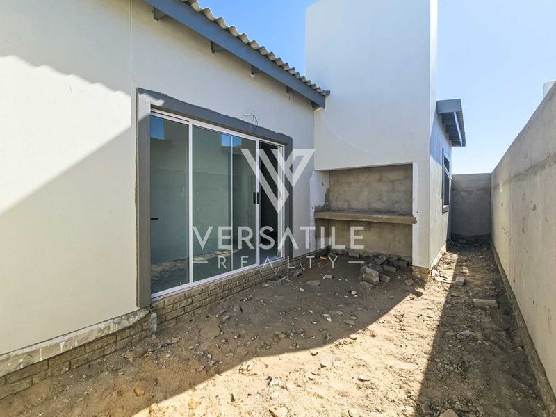 Rear exterior view of a townhouse featuring a built-in braai, sliding glass door access, and an unfinished garden area requiring landscaping.