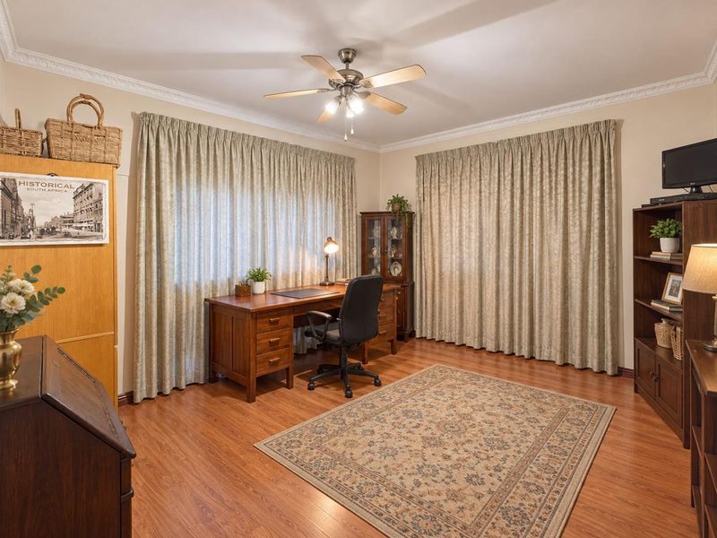 A well-maintained home office featuring laminate flooring, decorative cornice, and a ceiling fan, providing a functional and quiet workspace.