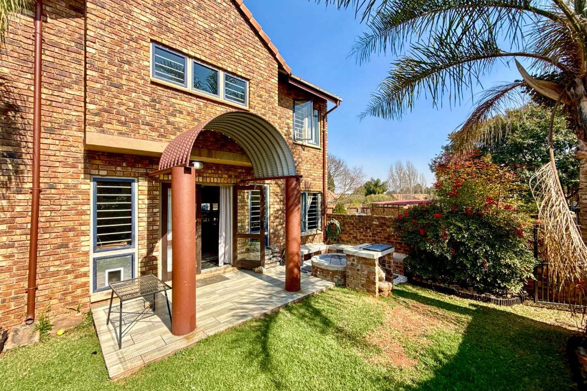 Rear view of the townhouse featuring a face brick facade, a covered patio with a built-in brick braai, and a private garden area.