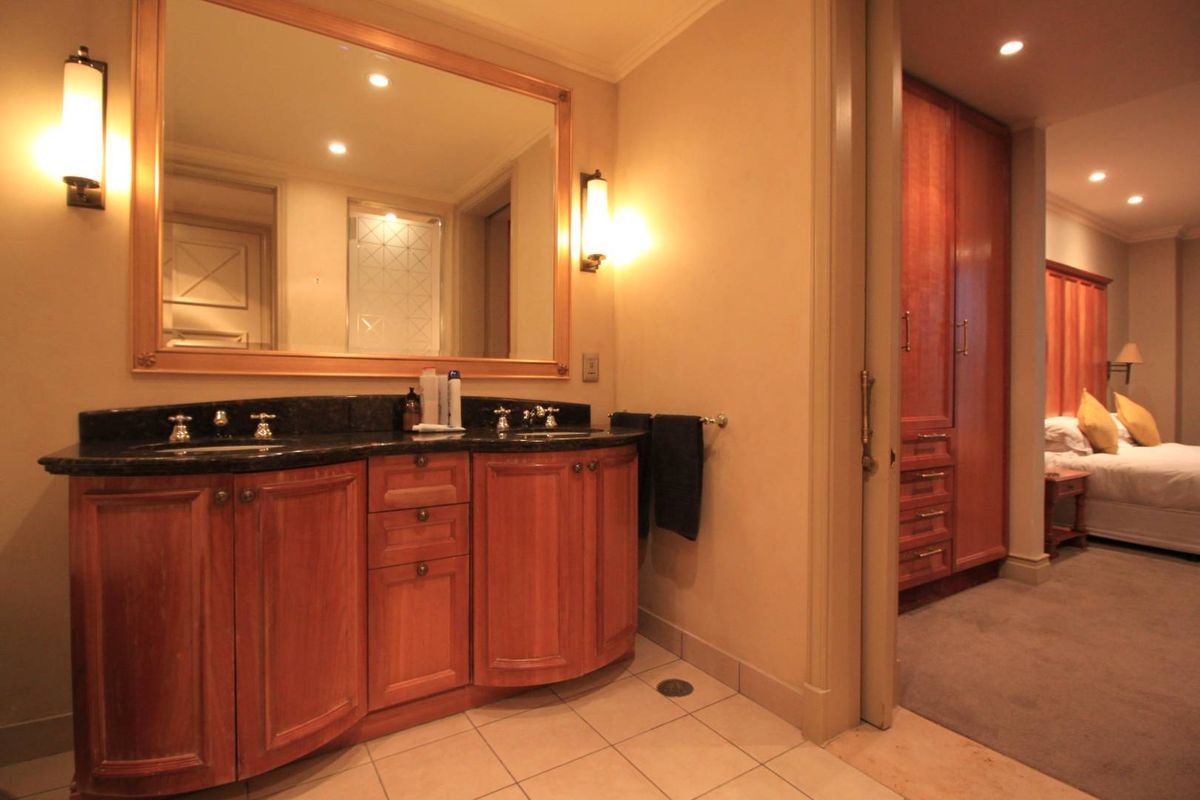 A well-appointed bathroom featuring a dual-sink vanity with dark stone countertops, wooden cabinetry, and a large framed mirror, adjacent to a bedroom area.