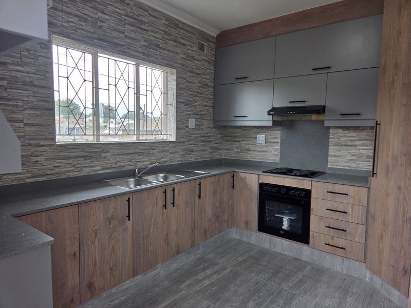 Modern kitchen featuring wood-grain and grey cabinetry, stone countertops, integrated oven and hob, and a double sink with a window view.