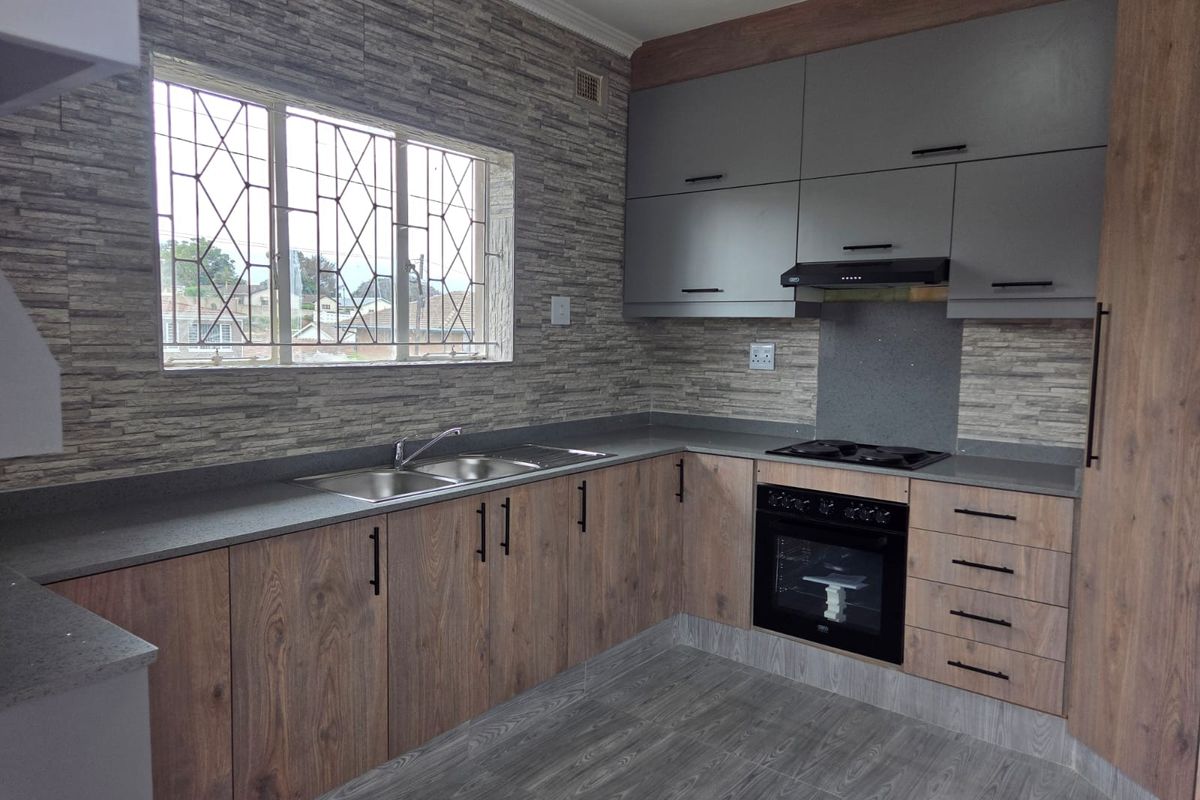 Modern kitchen featuring wood-grain and grey cabinetry, stone countertops, integrated oven and hob, and a double sink with a window view.