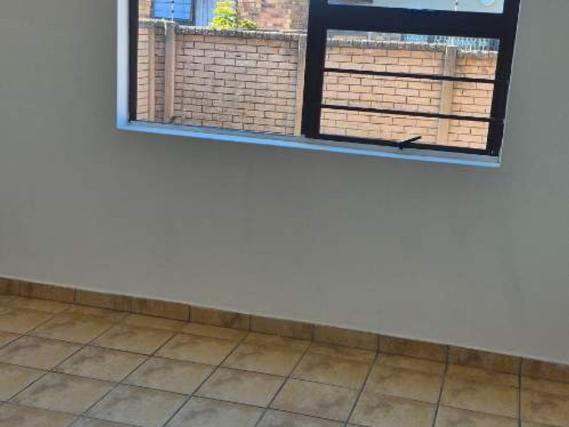 An empty bedroom featuring tiled flooring and a window fitted with security bars, offering a clean and neutral space ready for personalization.