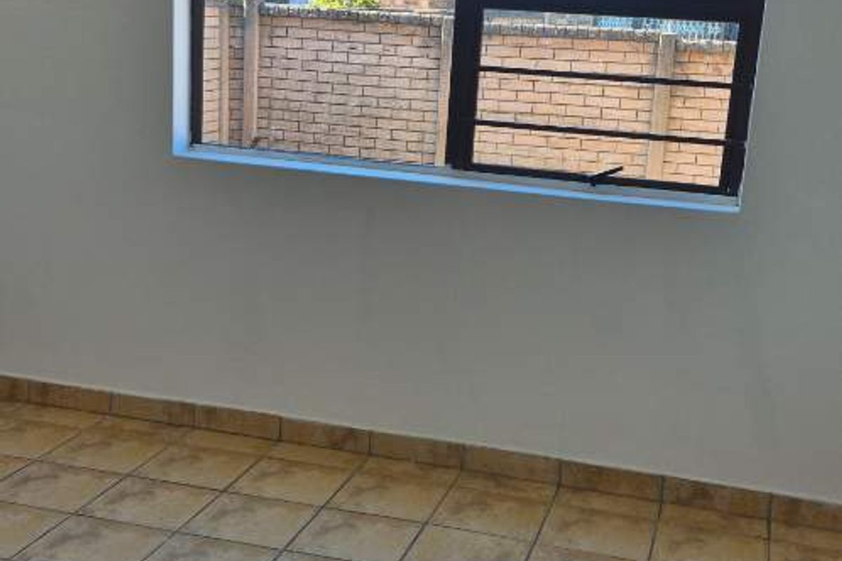 An empty bedroom featuring tiled flooring and a window fitted with security bars, offering a clean and neutral space ready for personalization.