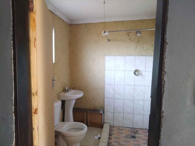 A basic bathroom featuring a pedestal basin, toilet, and tiled shower area, currently requiring significant cosmetic updates and repairs to finishes.