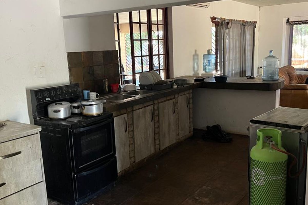 A dated kitchen featuring built-in cabinetry, a stone tile backsplash, and a breakfast bar, opening into an adjacent living area.