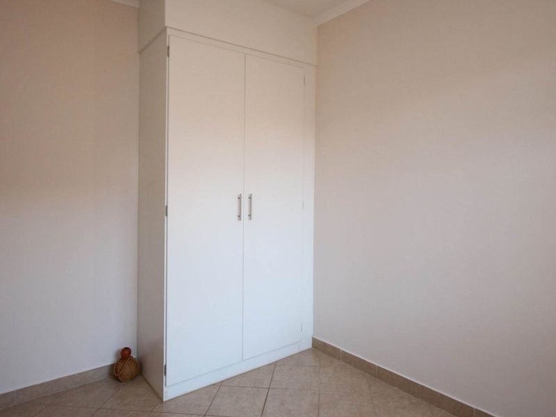 A clean, empty bedroom featuring neutral walls, tiled flooring, and a built-in white wardrobe.