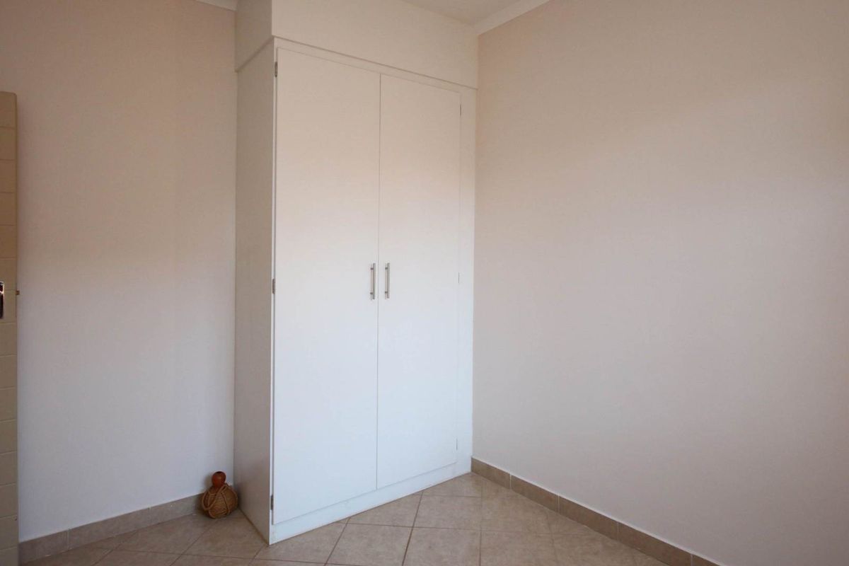 A clean, empty bedroom featuring neutral walls, tiled flooring, and a built-in white wardrobe.