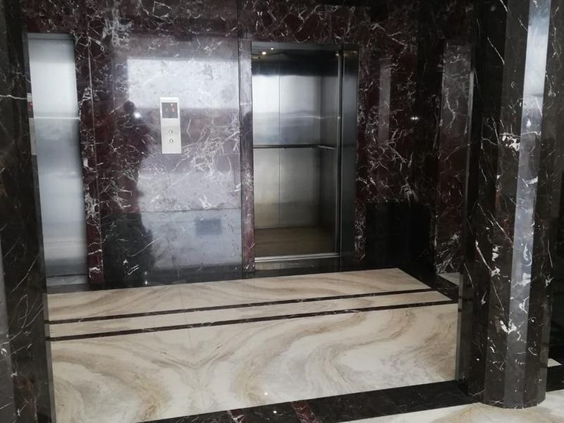 A modern office building lobby featuring high-end marble wall cladding and flooring with a functional elevator access point.