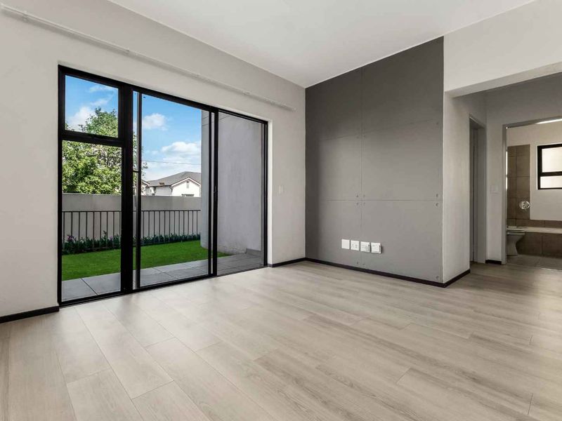 Bright and modern living area featuring light laminate flooring, a contemporary feature wall, and large sliding doors opening to a private garden space.