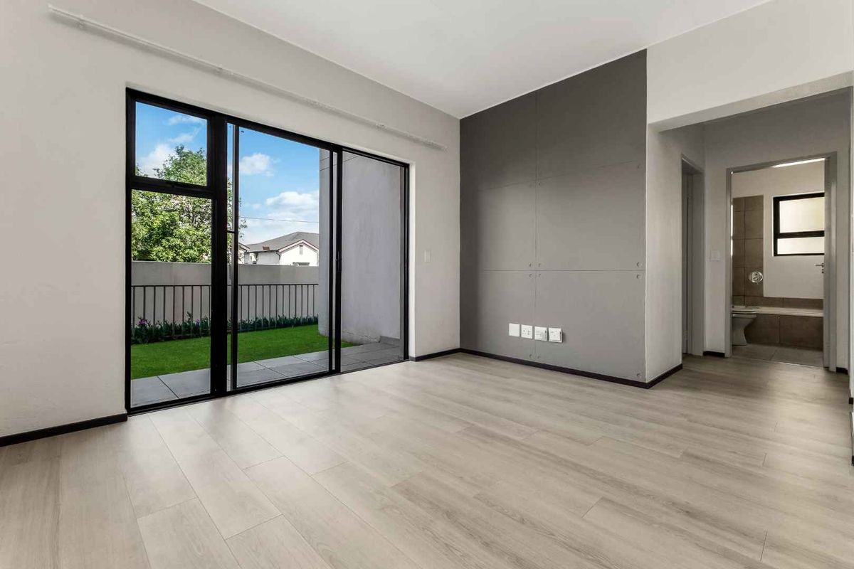 Bright and modern living area featuring light laminate flooring, a contemporary feature wall, and large sliding doors opening to a private garden space.