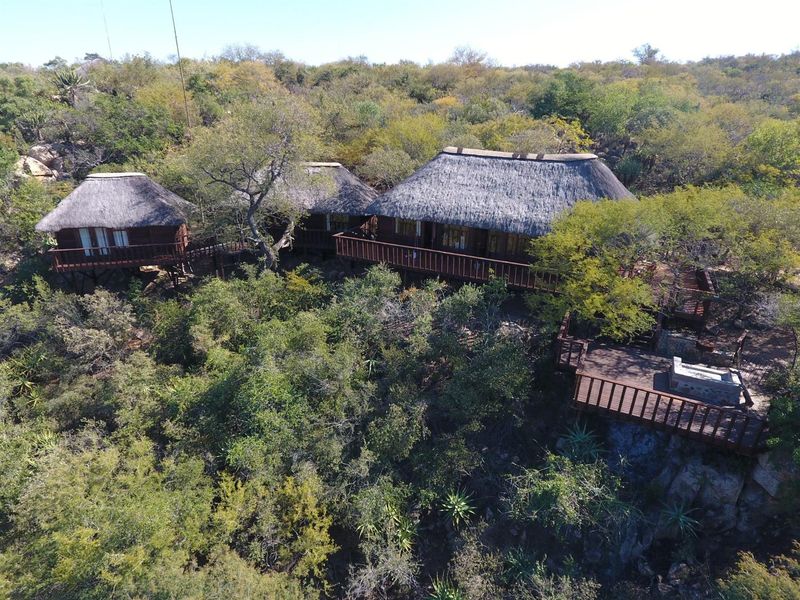 Aerial view of a bushveld lodge featuring multiple thatched-roof structures connected by elevated wooden walkways and decks set within a natural landscape.