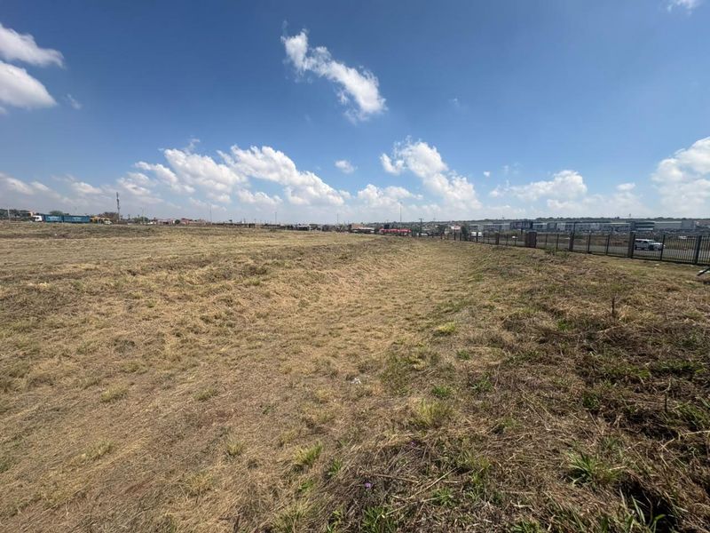 A wide-angle view of a vacant commercial land plot featuring perimeter fencing and open, cleared terrain under a clear sky.