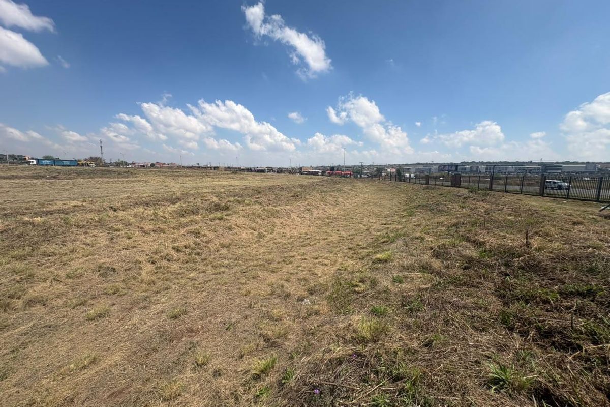 A wide-angle view of a vacant commercial land plot featuring perimeter fencing and open, cleared terrain under a clear sky.
