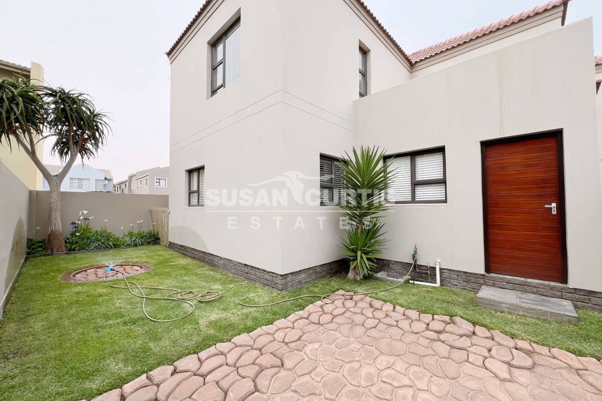 Rear view of the property featuring a paved patio area, a small landscaped garden, and a solid timber entrance door.