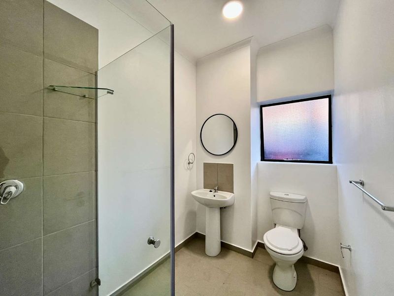 A clean, modern bathroom featuring a pedestal basin, a glass-enclosed shower with neutral tiling, and a toilet, finished with contemporary fixtures.