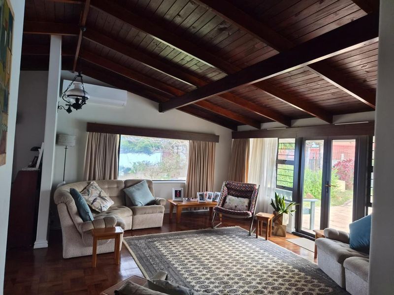Spacious living room featuring high exposed timber beam ceilings, rich parquet flooring, and large windows providing natural light and garden access.