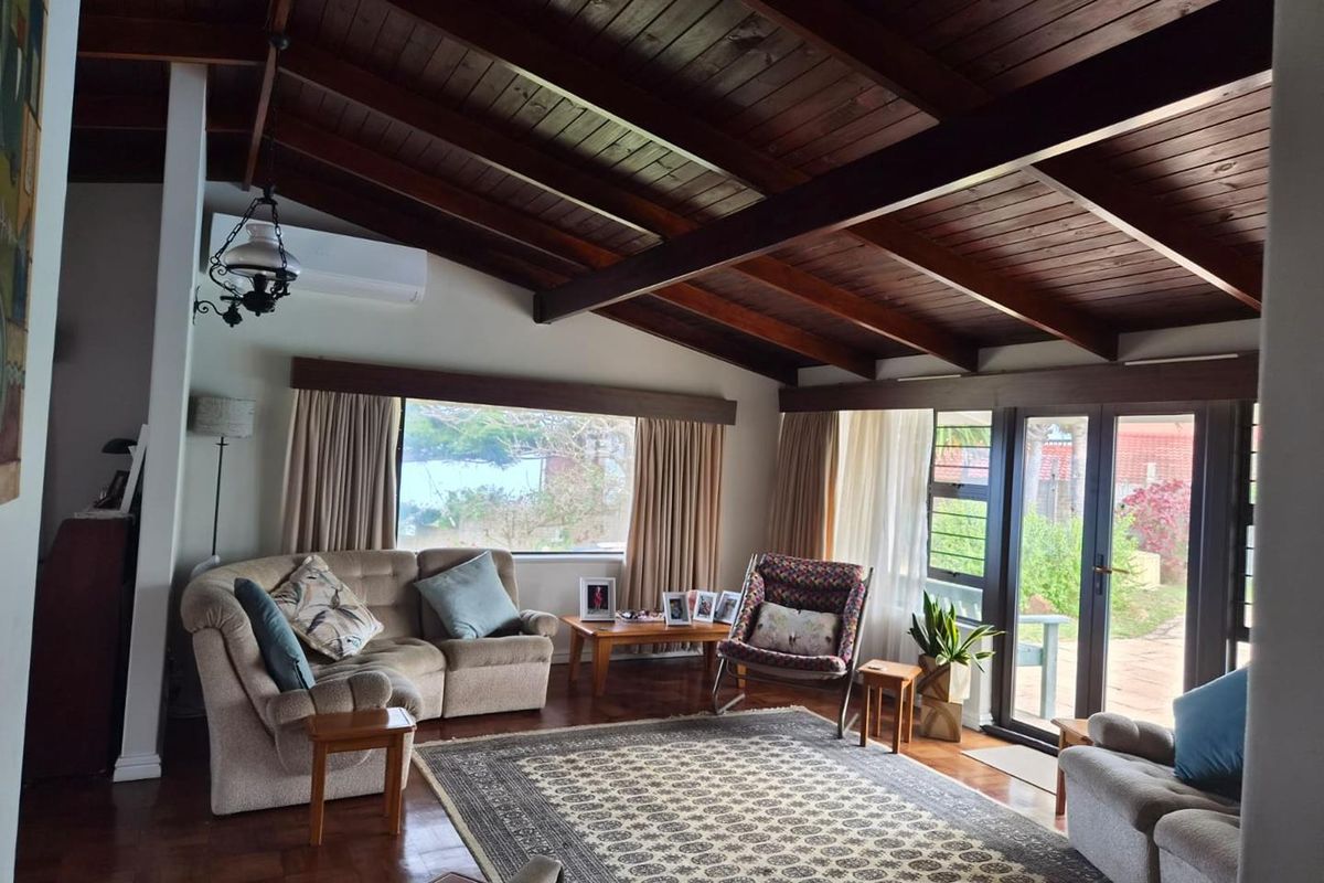 Spacious living room featuring high exposed timber beam ceilings, rich parquet flooring, and large windows providing natural light and garden access.