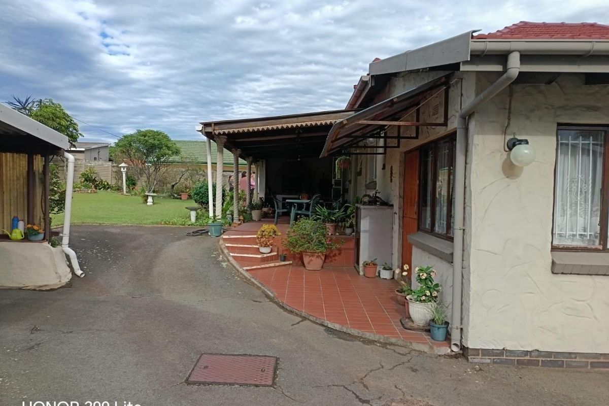 Rear view of the property featuring a covered tiled patio, asphalt driveway, and established garden area.
