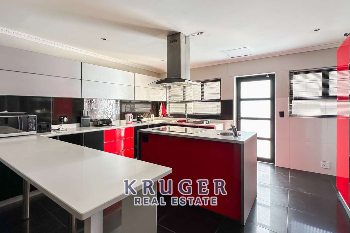 Modern kitchen featuring high-gloss red and white cabinetry, a central island with a prep sink, integrated hob, and stainless steel extractor fan.
