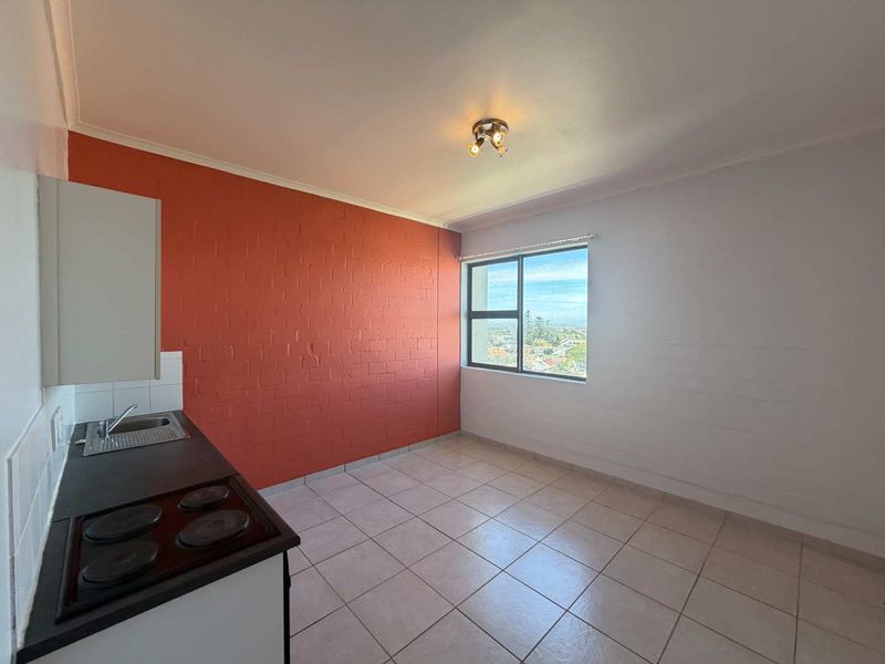 An empty kitchen area featuring tiled flooring, a built-in stove and hob, and a window with an exterior view.
