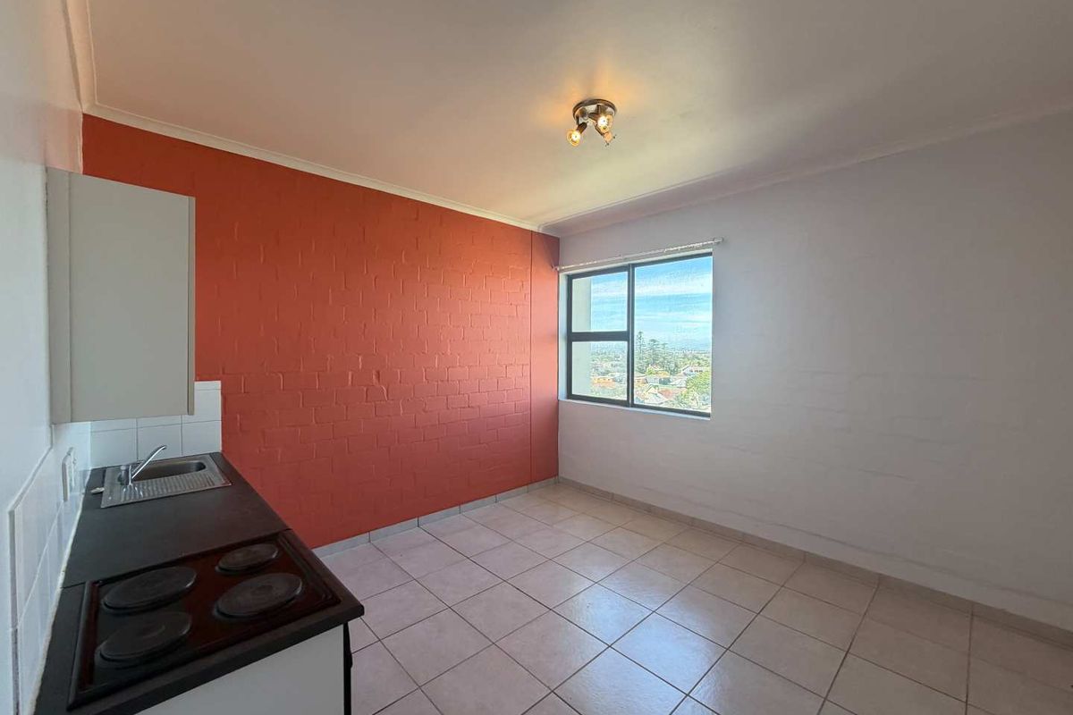 An empty kitchen area featuring tiled flooring, a built-in stove and hob, and a window with an exterior view.