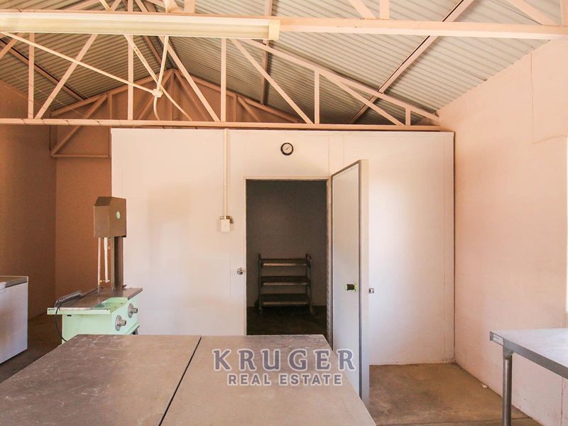 A functional utility or processing space featuring exposed roof trusses, industrial stainless steel work surfaces, and a built-in cold storage unit.