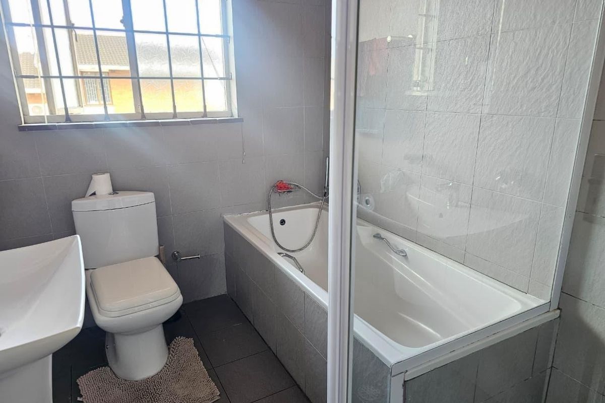 A functional bathroom featuring a bathtub with a shower screen, a pedestal basin, and a toilet, finished with neutral wall and floor tiles.
