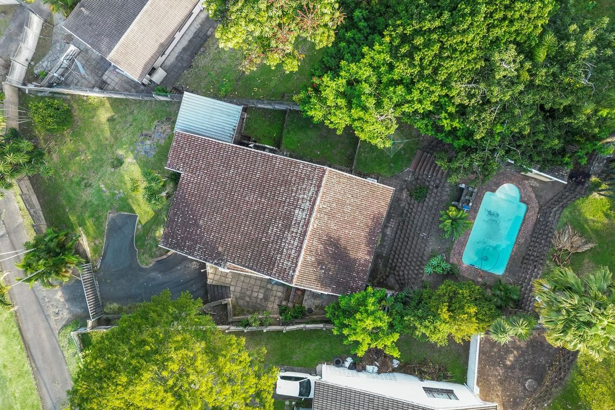 Aerial view of the property showing the main dwelling, swimming pool, paved patio area, driveway, and surrounding garden space.