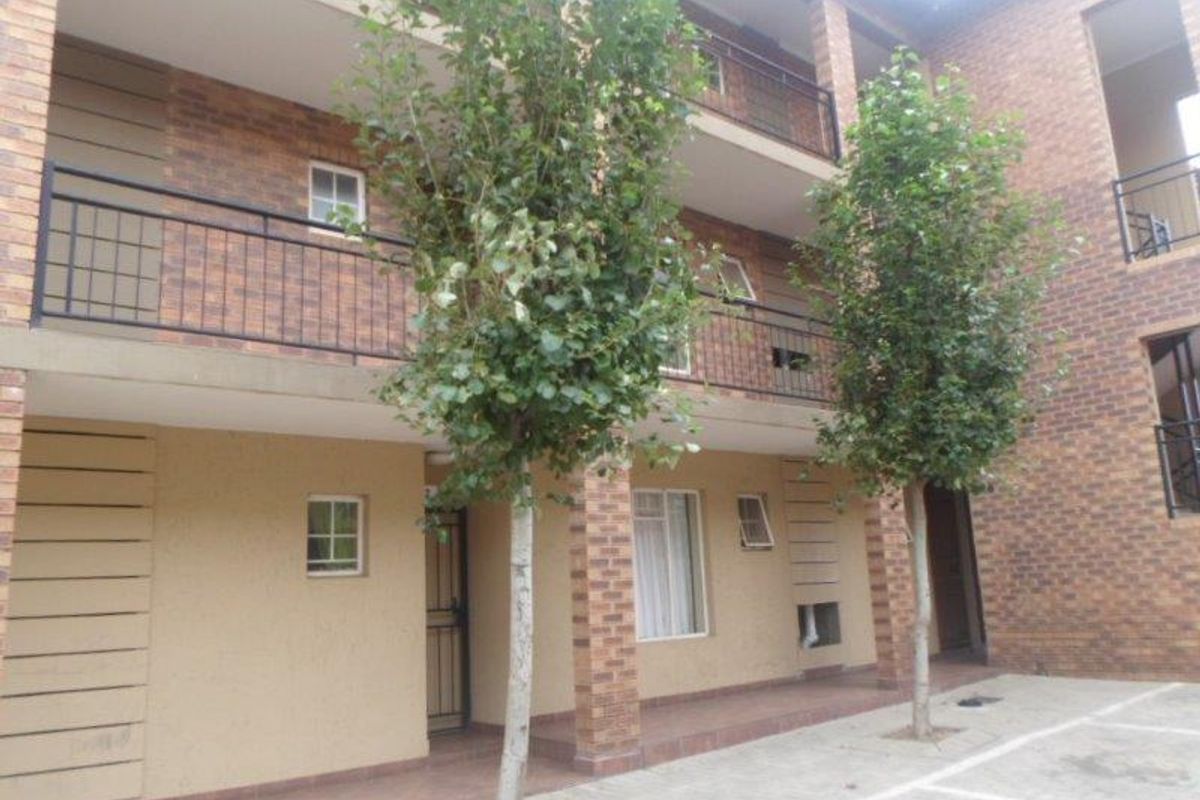 Exterior view of a multi-story apartment complex featuring face brick construction, covered patios, and a paved courtyard area.