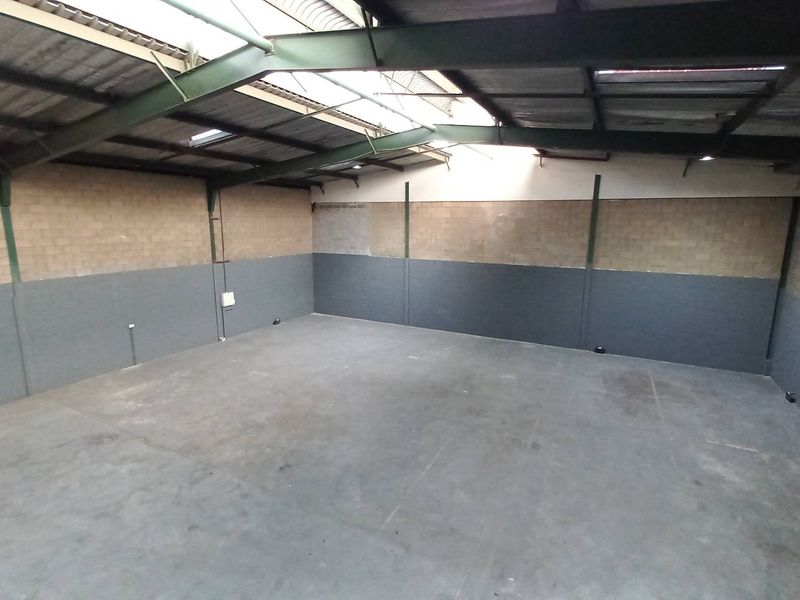 Spacious industrial warehouse unit featuring high ceilings with exposed steel trusses, concrete flooring, and dual-tone block walls with integrated skylights.