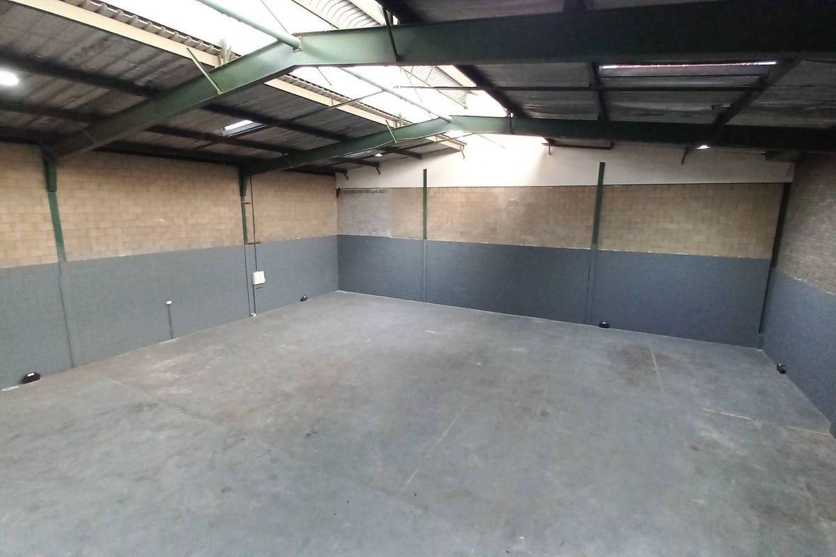 Spacious industrial warehouse unit featuring high ceilings with exposed steel trusses, concrete flooring, and dual-tone block walls with integrated skylights.